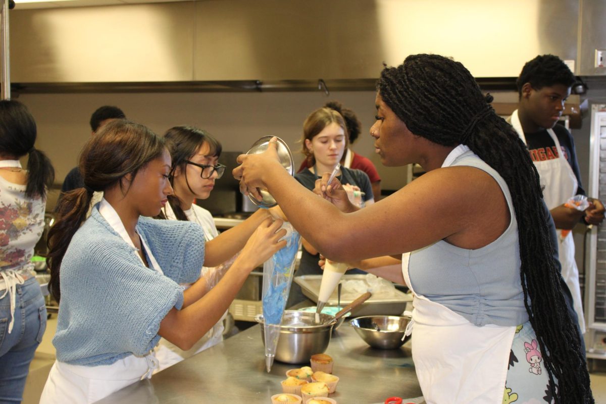 "Culinary students putting icing into an icing bag on top of their cupcakes"